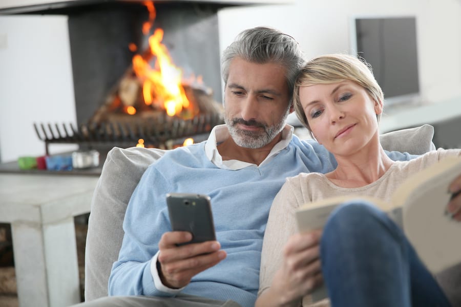 Middle-aged couple using smartphone at home by fireplace